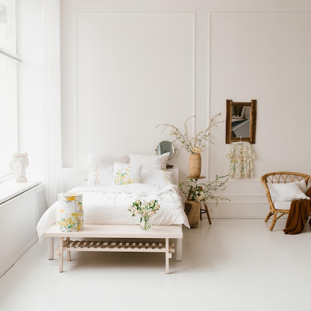 A bed in the bedroom with white linens spring yellow flowers in a vase on the bedside table