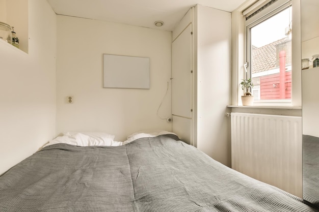 A bed in a room with a window and air conditions on the wall next to the bed is an electric heater