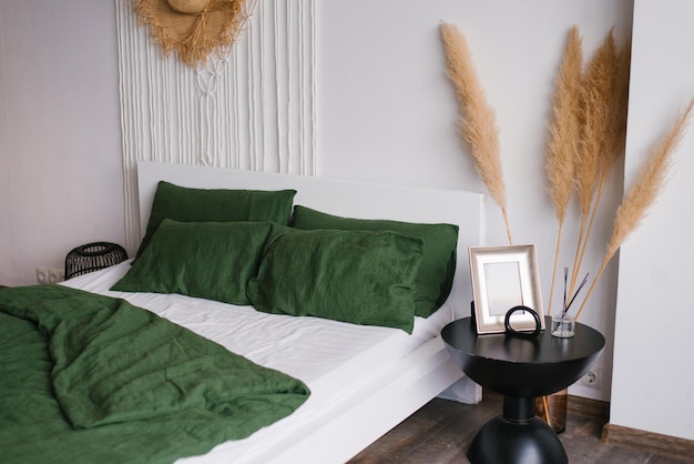 Bedroom in boho or rustic style White and green bed linen on the bed and dried flowers near the bedside table