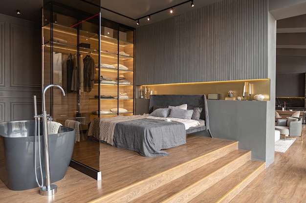 Bedroom and freestanding bath behind a glass partition in a chic expensive interior of a luxury home with a dark modern design with wood trim and led light