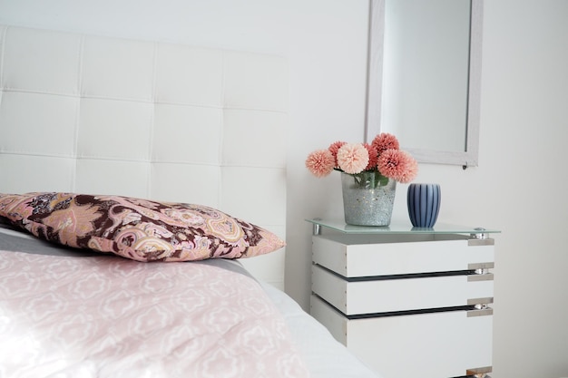 Bedroom interior design Mirror on the wall A bouquet of beautiful pink flowers on a white table in the bedroom Interior Design Bed with white upholstered headboard Decorative pillow