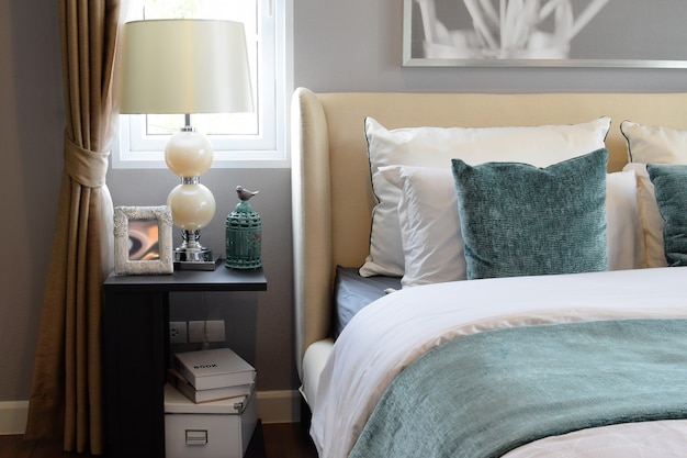 Bedroom interior design with white and green pillows on white bed and decorative table lamp.