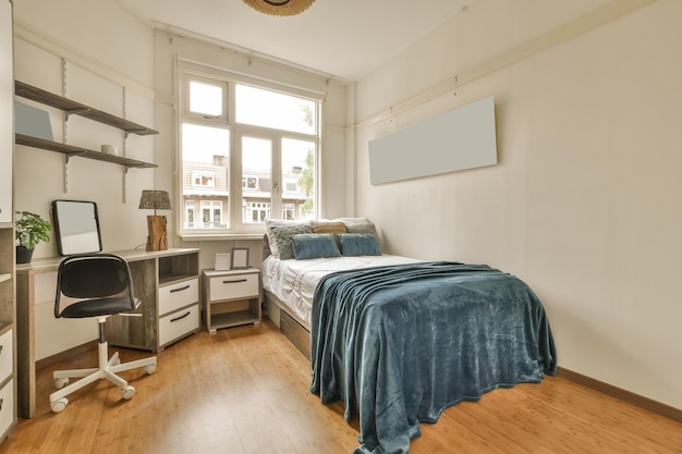 a bedroom with a bed desk and computer on the floor in front of the window looking out onto the street