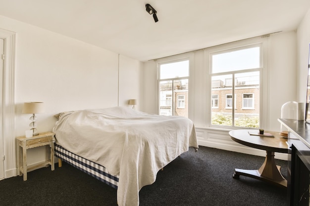 A bedroom with a bed desk and television set in the corner next to the window looking out onto the street