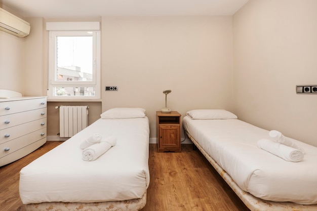 Bedroom with twin beds with white duvet white chest of drawers and chestnut wood floors