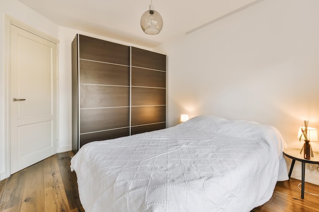 a bedroom with wood flooring and white comforter on the bed in front of the door to the room