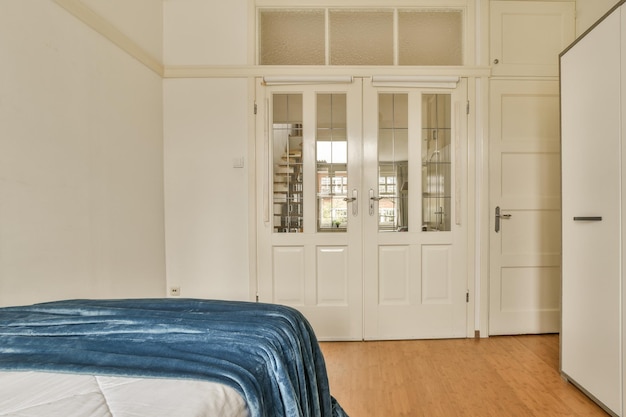 a bedroom with wood flooring and white door leading to another room that has a blue blanket on the bed