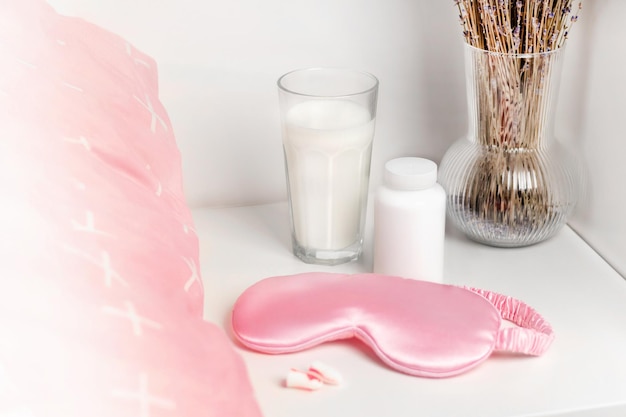 Bedside table with a silk sleep mask earplugs and lavender and warm milk for a good nights sleep and sleeping pill mock up All conditions for good deep sleep Help for falling asleep