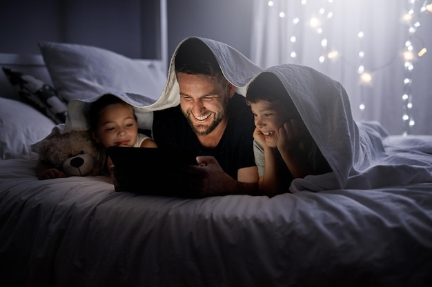 Bedtime just turned in to the best time Shot of a father and his two little children using a digital tablet together in bed at night