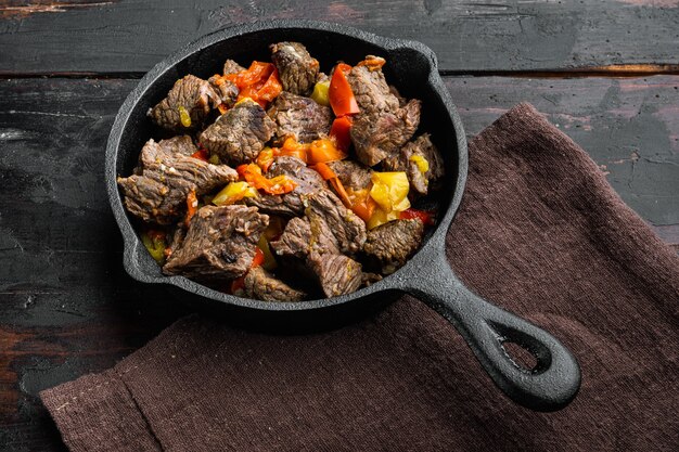 Photo beef bourguignon stew with vegetables set, in cast iron frying pan, on old dark wooden table