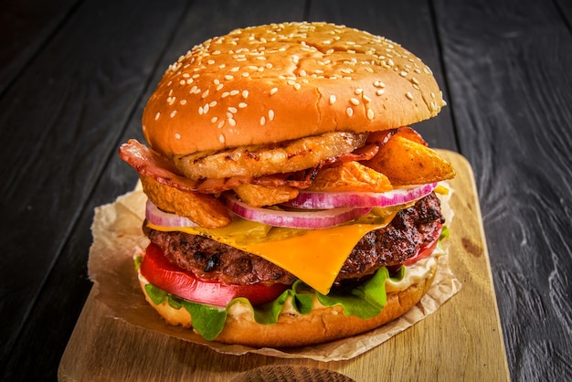 Beef burger with melted cheese and bacon on wooden background.