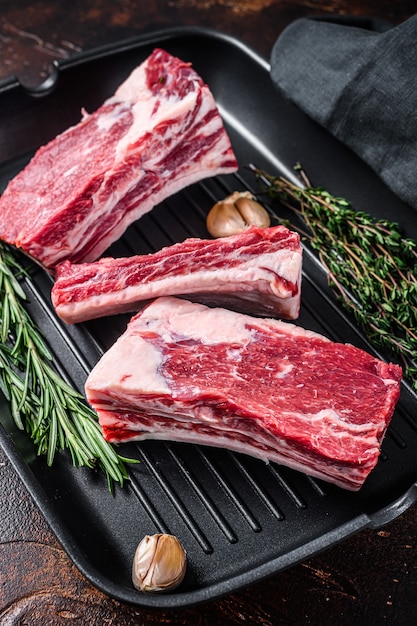 Beef calf short ribs meat in a grill pan ready for cooking. Dark background. Top view.