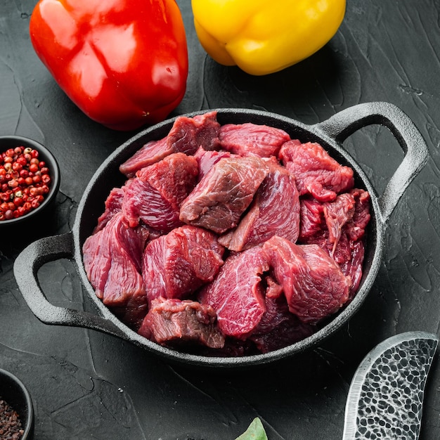 Beef casserole or goulash ingredients with sweet bell pepper in cast iron frying pan on black stone background