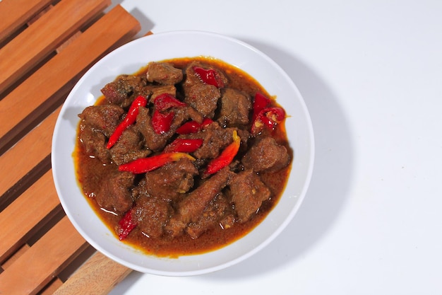 beef cooked in rendang with a garnish of cayenne pepper served on a white plate and wooden coaster