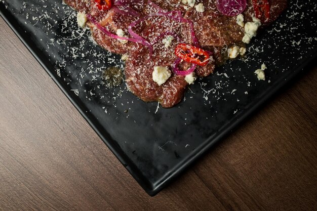 Beef fillet carpaccio with red pepper onions parmesan cheese on a black plate Carpaccio