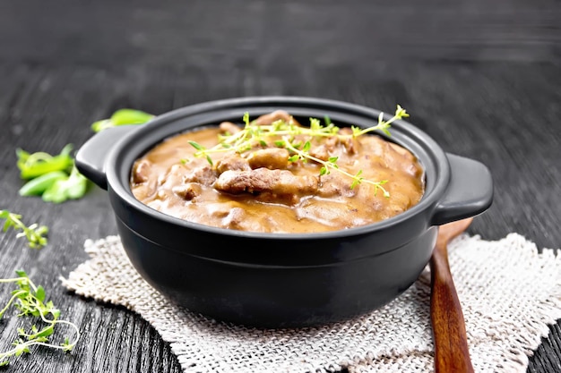 Beef goulash in tomato sauce with thyme sprigs in a pan on burlap spoon parsley on wooden board background