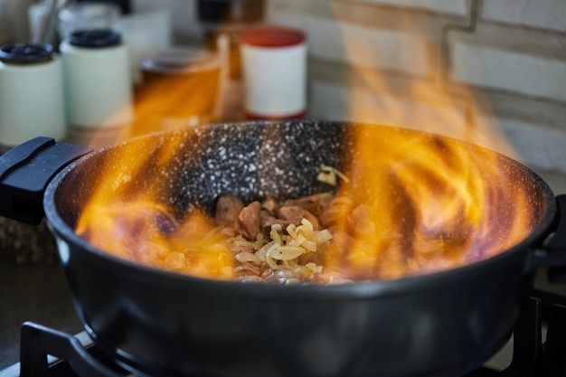 Beef meat fried with onions in frying pan flambe on gas stove