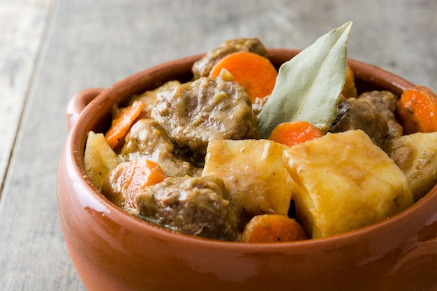 Beef meat stewed with potatoes, carrots and spices in bowl on wooden table