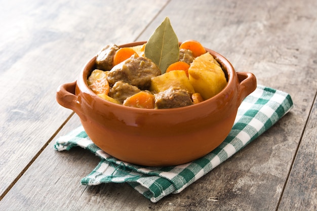 Beef meat stewed with potatoes, carrots and spices in bowl on wooden table