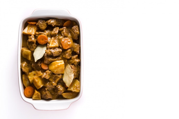 Beef meat stewed with potatoes, carrots and spices in ceramic pot isolated on white background Top view