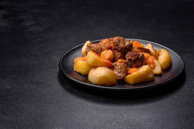 Beef meat and vegetables stew on a black plate with roasted potatoes