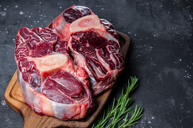 Beef meat witch bone on a cutting board with rosemary on the dark gray background close up. High quality photo