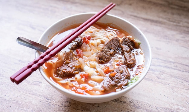 Beef noodle ramen meal with tomato sauce broth in bowl on bright wooden table famous chinese style food in Taiwan close up top view copy space