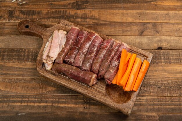 Beef roll raw to prepare with bacon and carrots on a kitchen board