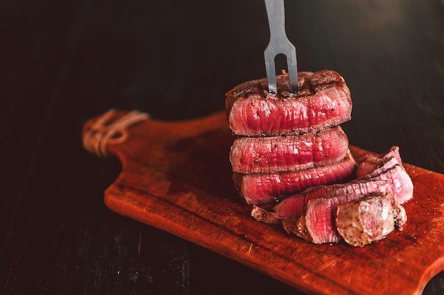 Beef steak on a fork on a dark wooden surface