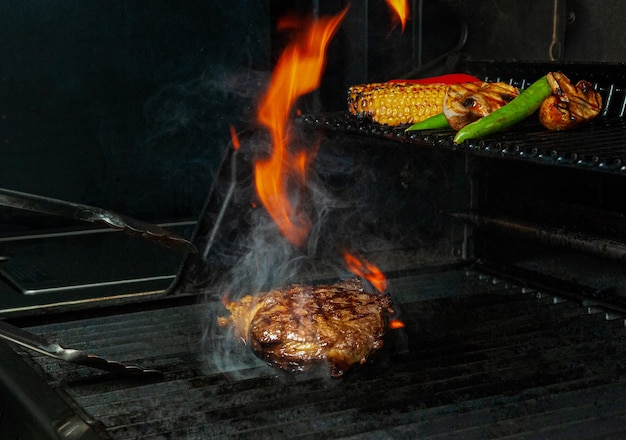 Beef steak and vegetables are grilled and turned over with tongs