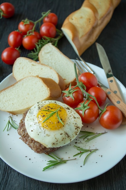 Beef steak with fried egg in spices served on a white plate. American dish. Dark wooden background. Side view. Close-up.