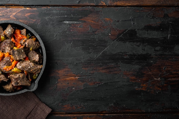 Beef stew goulash - rustic style set, in cast iron frying pan, on old dark wooden table, top view flat lay