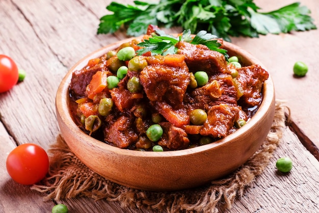 Beef stew meat ragout with carrots onions and green peas vintage wooden background selective focus