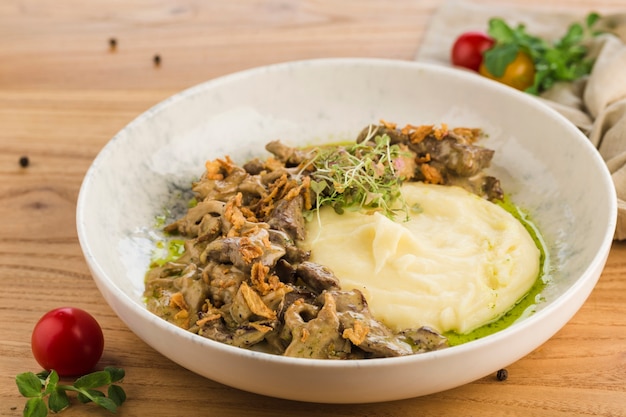 Beef stroganoff with mashed potatoes in a plate on a light wooden surface.