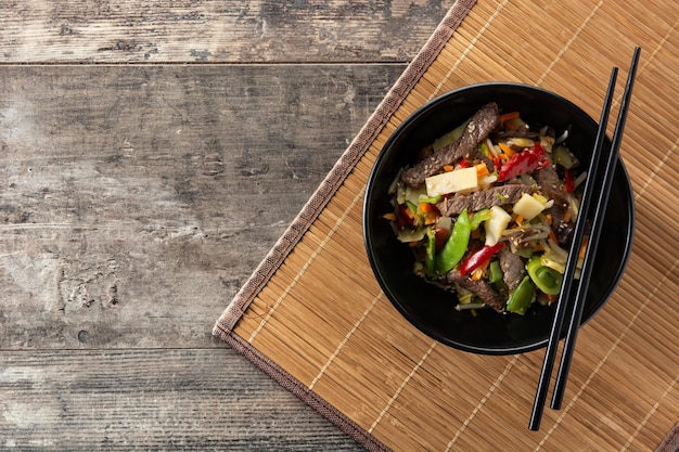 Beef, vegetables and sesame seeds in black bowl on wooden table