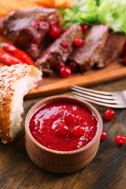 Beef with cranberry sauce roasted potato slices on cutting board on wooden background