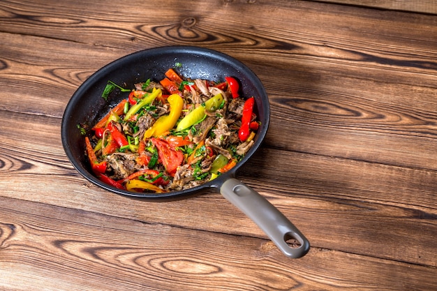 Beef with vegetables in a frying pan on a wooden background. Top view