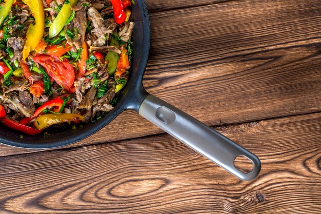 Beef with vegetables in a frying pan on a wooden background. Top view