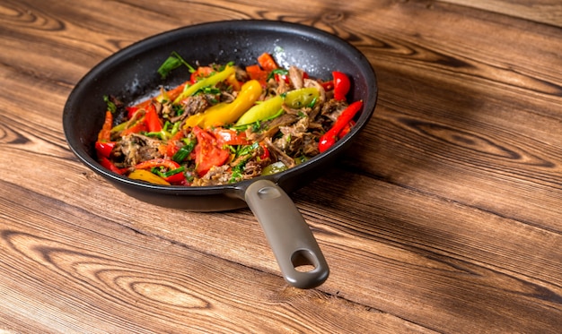 Beef with vegetables in a frying pan on a wooden background. Top view