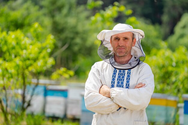 The beekeeper stands crosshands near apiary. Apiculture. Apiary.