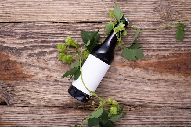 Beer bottle lies on wooden background with hop cones close up White label mock up