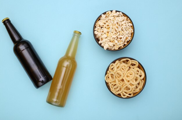 Beer bottles and bowls with snacks on blue background. Top view