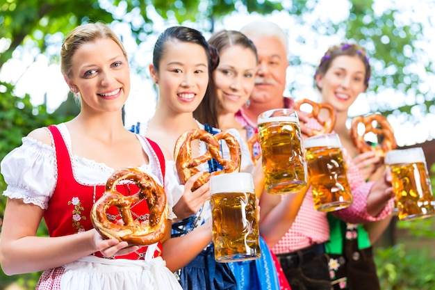 In Beer garden - friends, man and women in Tracht, Dirndl and Lederhosen drinking a fresh beer in Bavaria, Germany