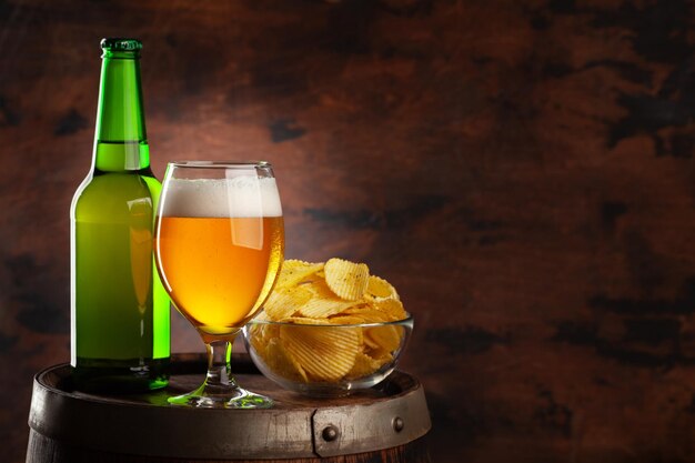 Beer glass bottle and chips on wooden barrel