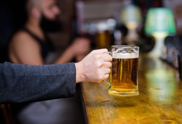 Beer mug on bar counter defocused background. Glass with fresh lager draft beer with foam. Male hand holds mug filled with cold tasty beer in bar. Friday leisure tradition. Beer pub concept.