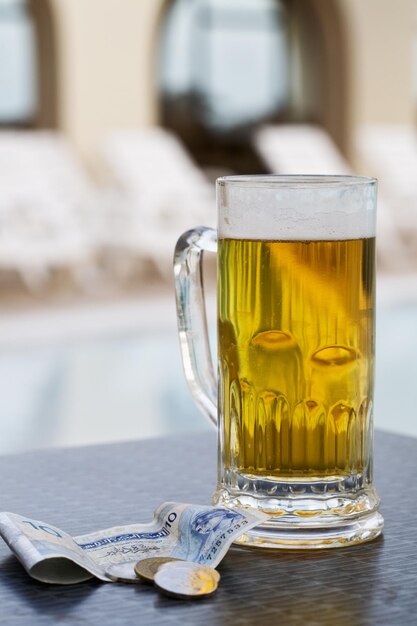 Beer mug and currency by swimming pool in tropical resort