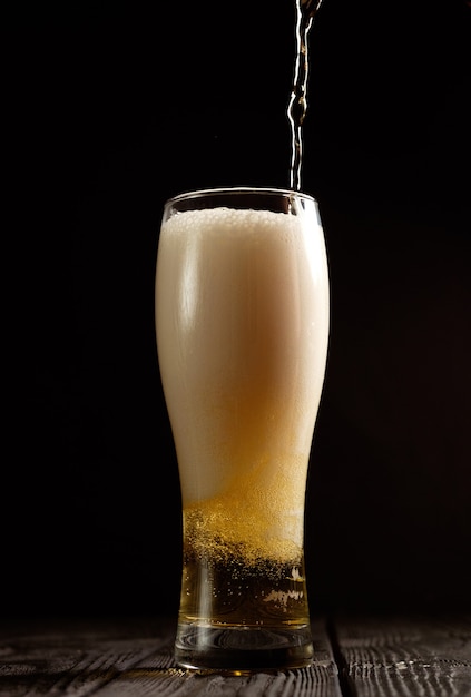 Beer pours into glass on black background