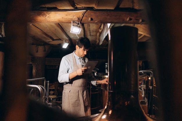 Beer quality control Man in apron and protective mask with digital tablet looking at glass of beer on brewery factory free space