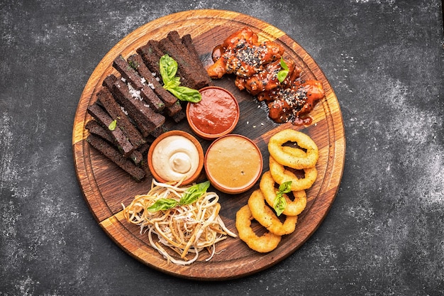 Beer snack on a wooden board onion rings croutons squid grilled chicken wings and sauces