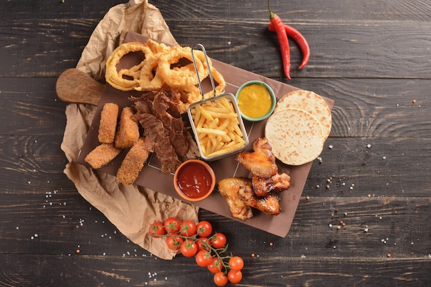 Beer snacks. Fried chicken wings, french fries, onion rings, cheese in batter and dried meat. On a wooden board